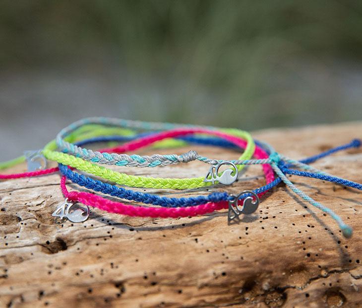 4ocean Dolphin Braided Anklet - light blue multi color. On drift wood with 3 other 4ocean braided anklets.