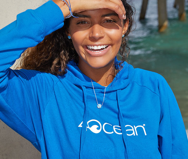 The 4ocean long sleeve hoodie in blue. The hoodie is on a female model and has the 4ocean logo on the front in white.