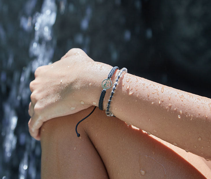 A female modeling our crew bracelet and shark beaded bracelet with the waterfall in the background 