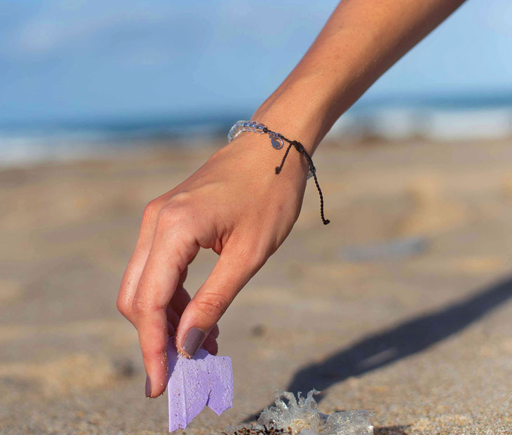 The shark beaded bracelet being modeled by a female picking up a piece of plastic