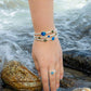 A person wearing a Dune Bali bracelet and a Dune Bali ring with her hand in the water at the beach