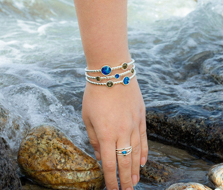 A person wearing a Dune Bali bracelet and a Dune Bali ring with her hand in the water at the beach