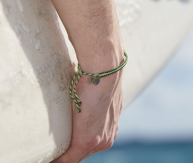 4ocean Earth Day Braided Bracelet 2022 - green. On male model with surf board.
