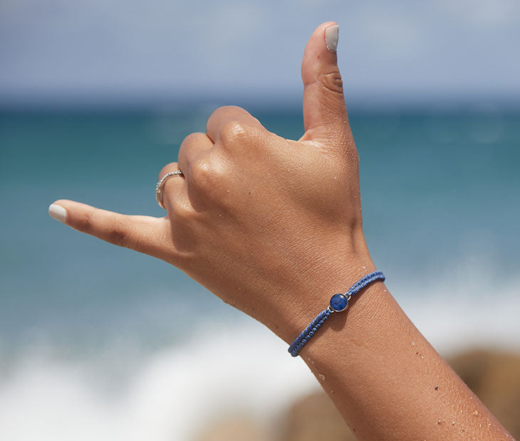 Ocean Drop Bracelet, Black and Blue modeled on a females hand with the ocean in the background