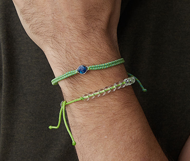 4ocean Green Ocean Drop Bracelet. Green and yellow cord with attached blue and stainless bezel. Shown on male model with coordinating green beaded bracelet.