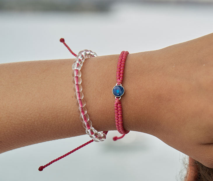 4ocean Pink Ocean Drop Bracelet. Pink braided cord with stainless and blue bezel. Shown on female model with a coordinating 4ocean beaded bracelet.