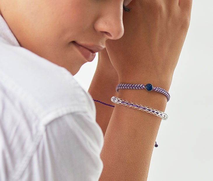 4ocean Purple Ocean Drop Bracelet. Purple braided cord with stainless and blue bezel. Shown on female model with coordinating 4ocean purple beaded bracelet.