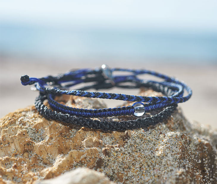 Shark Bracelet stack being displayed to showcase that 3 braided bracelets in our signature blue and black colors can be worn together as one or individually on a piece of driftwood