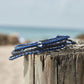 Shark Bracelet stack sitting on top of a wooden column with the beach background blurred out