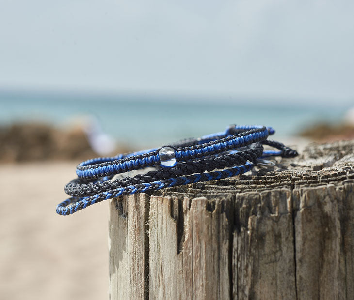 Shark Bracelet stack sitting on top of a wooden column with the beach background blurred out