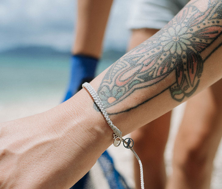 Tiger Shark braided bracelet being modeled on the beach by a female with artistic arm tattoos